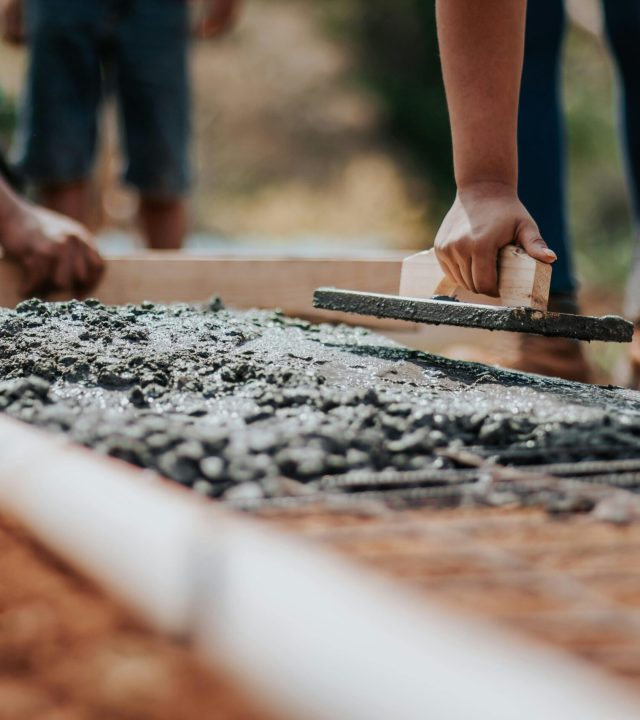 Construction workers leveling fresh cement on a sunny day at an outdoor site.